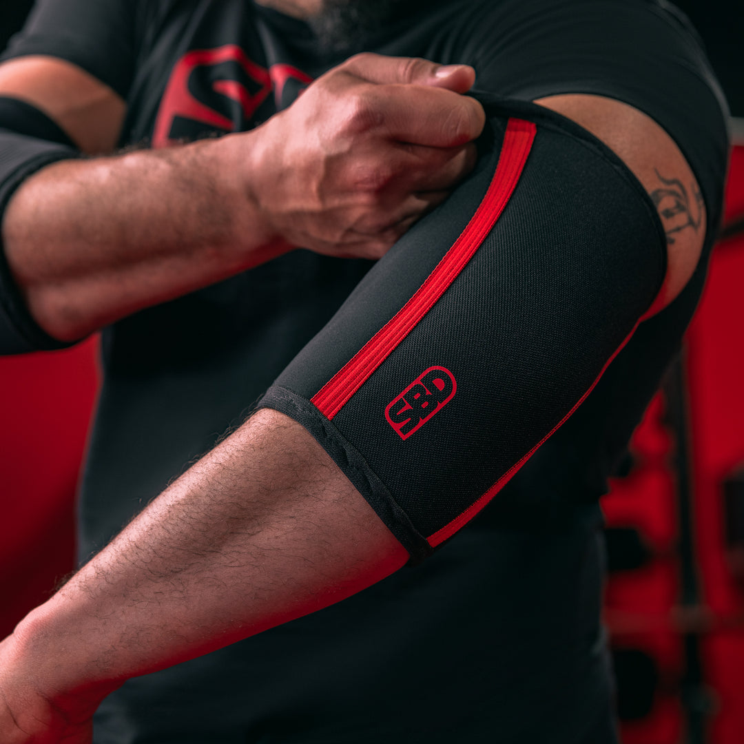 SBD Elbow Sleeves – zwart-rode sleeve wordt rond de elleboog aangetrokken