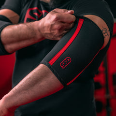 SBD Elbow Sleeves – zwart-rode sleeve wordt rond de elleboog aangetrokken