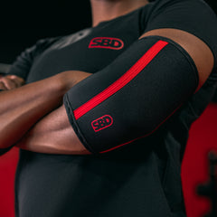 SBD Elbow Sleeves – zwart-rode sleeve gedragen om een gebogen elleboog