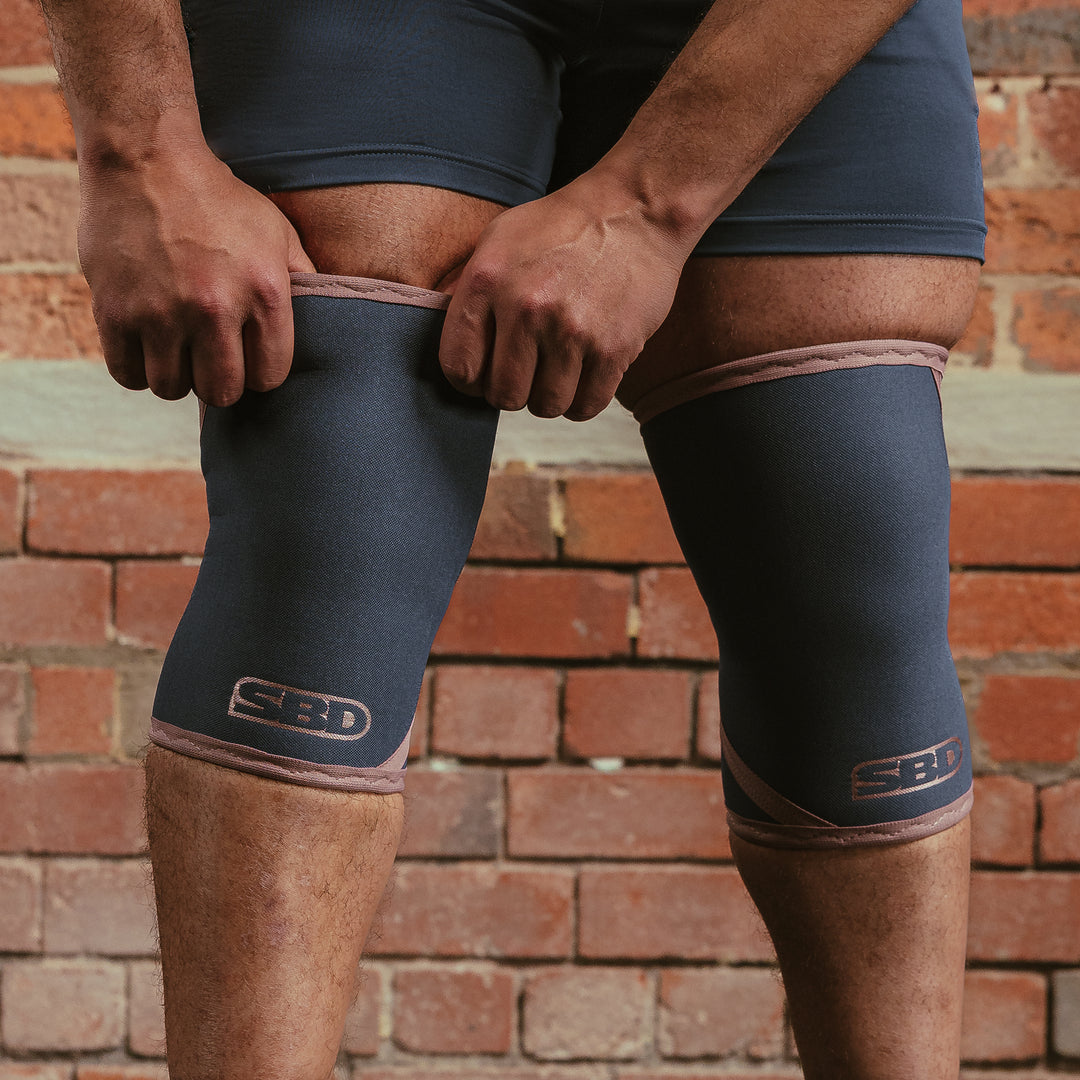 SBD Knee Sleeves 7mm - Serenity Limited Edition – blauwgrijze sleeves met roze afwerking gedragen door een man