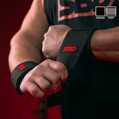 SBD Wrist Wraps – zwarte Stiff wrap met rood logo wordt aangebracht, met aanduiding