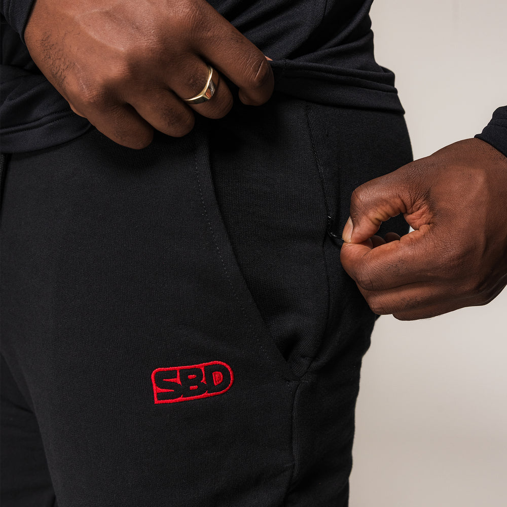 Detail van de ritszak en het rode SBD-logo op de zwarte SBD Joggers