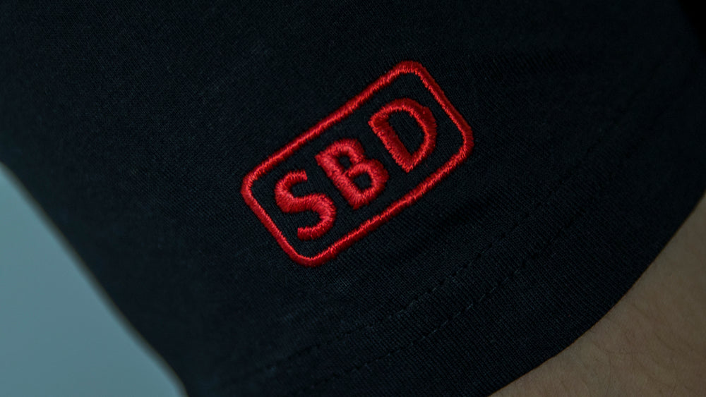 SBD T-Shirt – detail van het rode SBD-logo op zwarte stof
